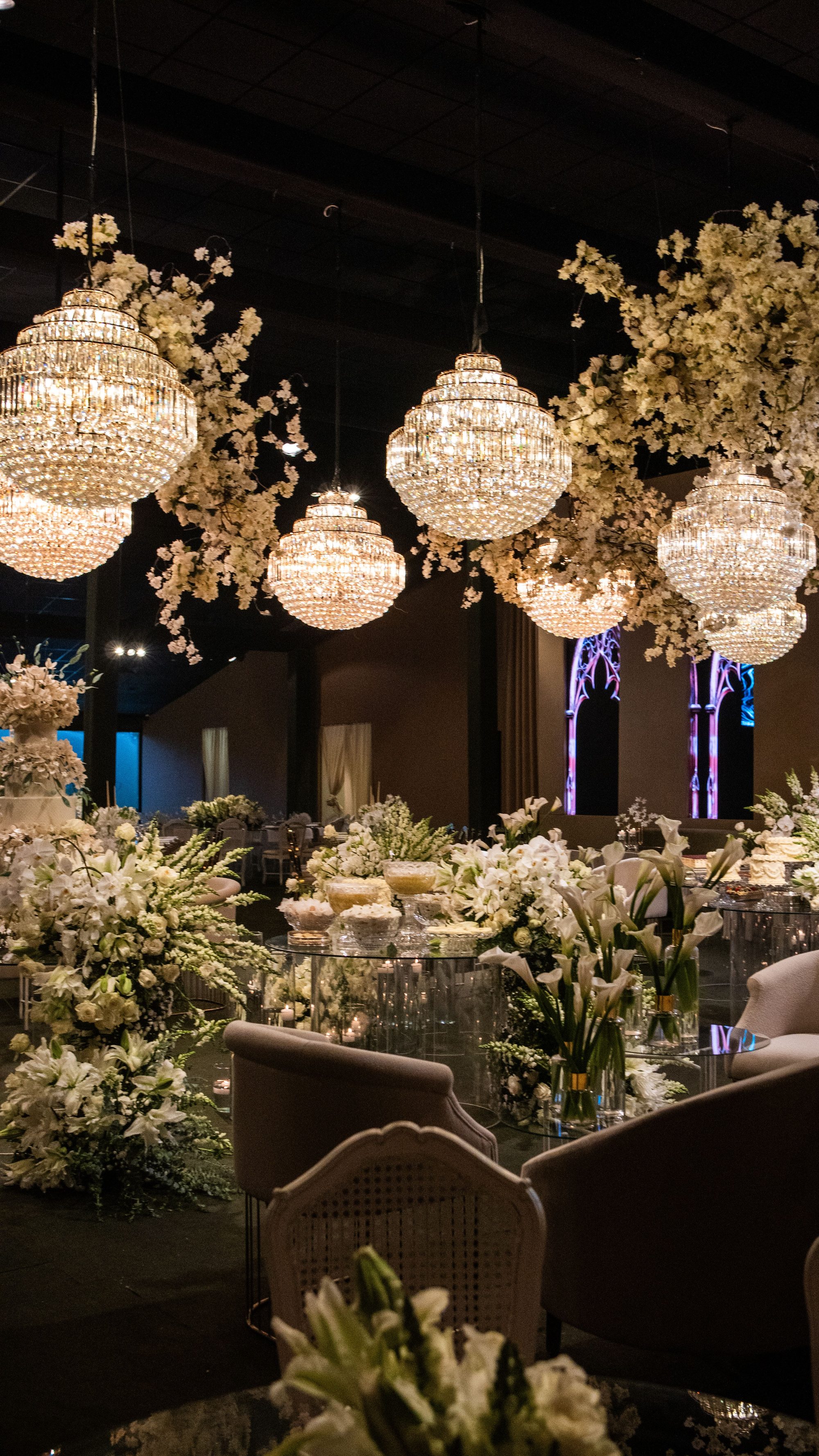 Dessert table beneath crystal chandeliers with white floral arrangements at an evening reception